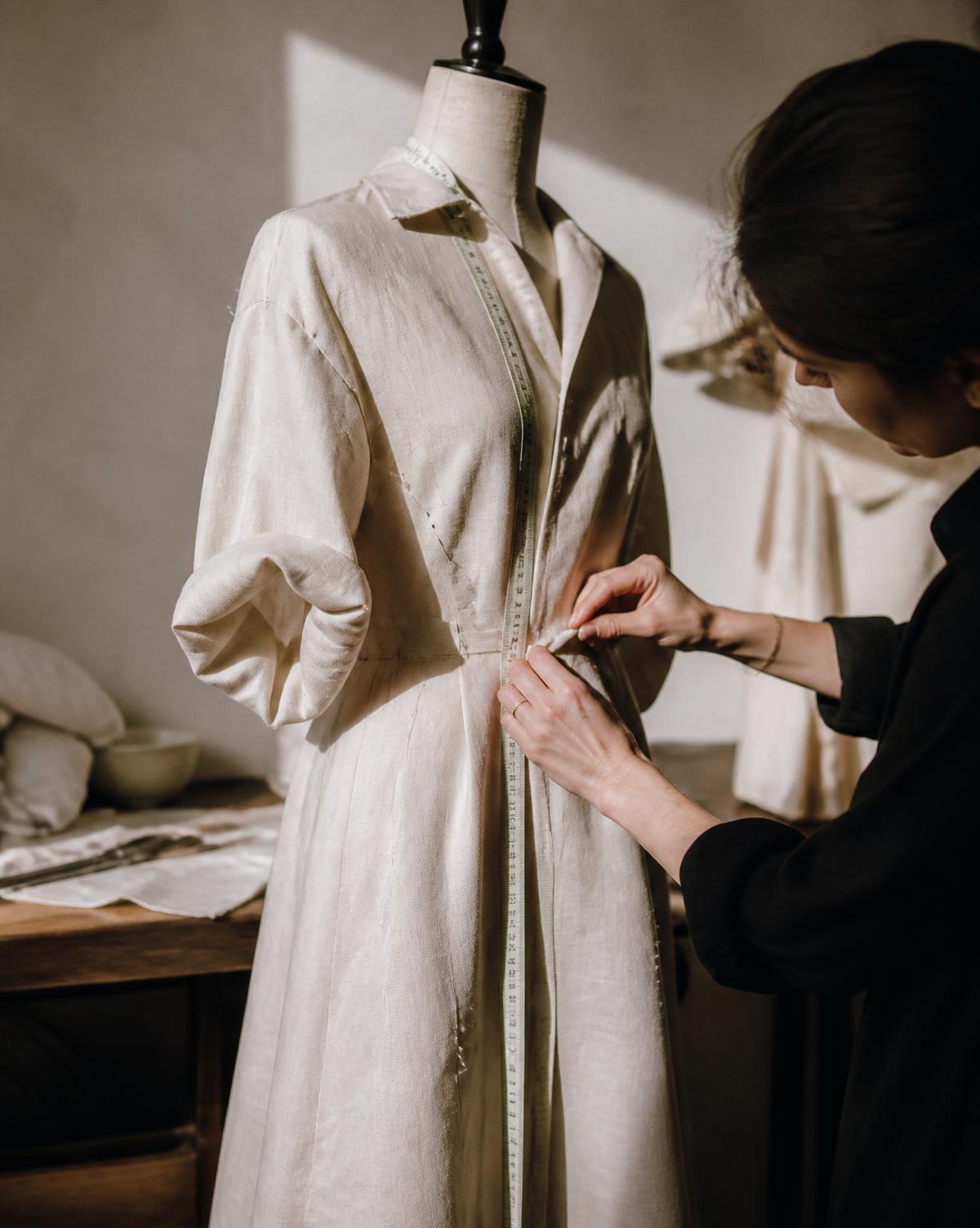 Robe-chemise en lin épinglée sur un buste, mains d'une couturière prenant une mesure